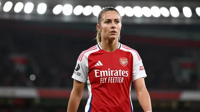 A mid-30s female Arsenal player, waist-up, wearing a solid red kit, focused expression, background blurred stadium...