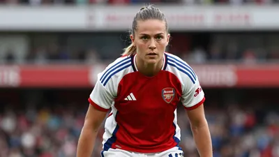 Mid-30s athletic female footballer, waist-up, intense gaze, wearing Arsenal Women home kit - red shirt with white...