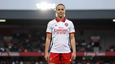 A 28-year-old female Arsenal Women player, wearing a white jersey with a red collar, a red pair of shorts, and a pair of...