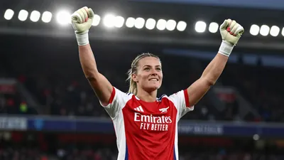 A tight action shot of an anonymous Arsenal Women player in a red and white kit, celebrating with arms raised after a...