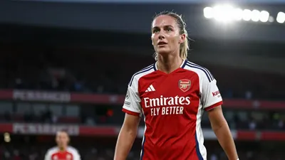 Floodlight rim light: A confident Arsenal Women midfielder in vibrant red and black kit stands triumphantly, sweat...