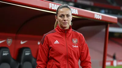 A tight action crop of an anonymous Arsenal Women coach in a bright red tracksuit, with a confident expression, standing...