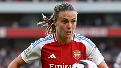 A close-up shot of an Arsenal Women player in a red jersey with white sleeves, running with the ball, surrounded by a...